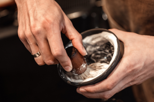 Person swirling a shaving brush into a shaving soap in a bowl