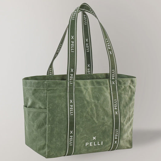 An olive green canvas tote bag with matching shoulder straps featuring a repeating white 'PELLI X PELLi' logo pattern, shown on a light gray background.